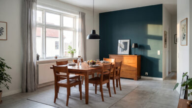 Esszimmer mit Esstisch und Stühlen aus Kirschbaum, dahinter eine Kirschbaum-Kommode vor einer blaugrünen Akzentwand, Nachmittagssonne durch ein großes Fenster