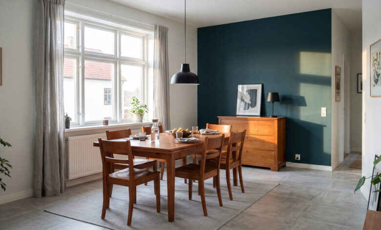 Esszimmer mit Esstisch und Stühlen aus Kirschbaum, dahinter eine Kirschbaum-Kommode vor einer blaugrünen Akzentwand, Nachmittagssonne durch ein großes Fenster