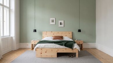 Zirbenbett mit zwei Nachttischen vor blassgrüner Wand, tannengrüne Decke und schwarze Pendelleuchten im Schlafzimmer